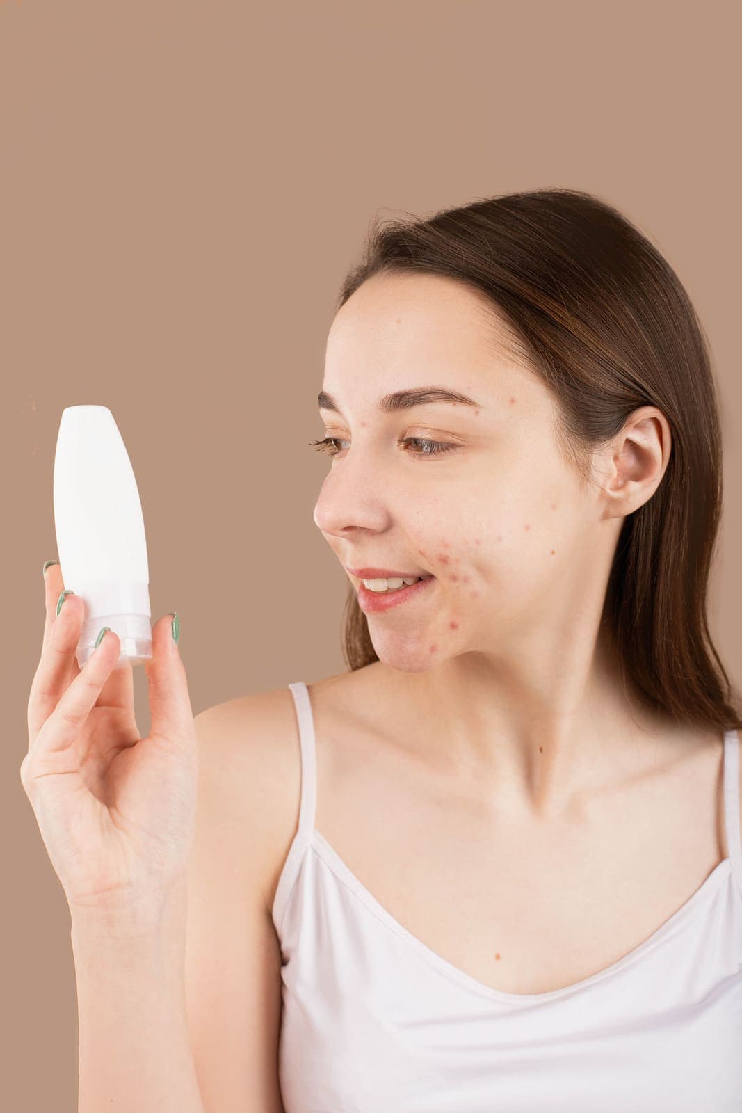 A smiling woman holding a skincare product formulated for acne-prone skin.