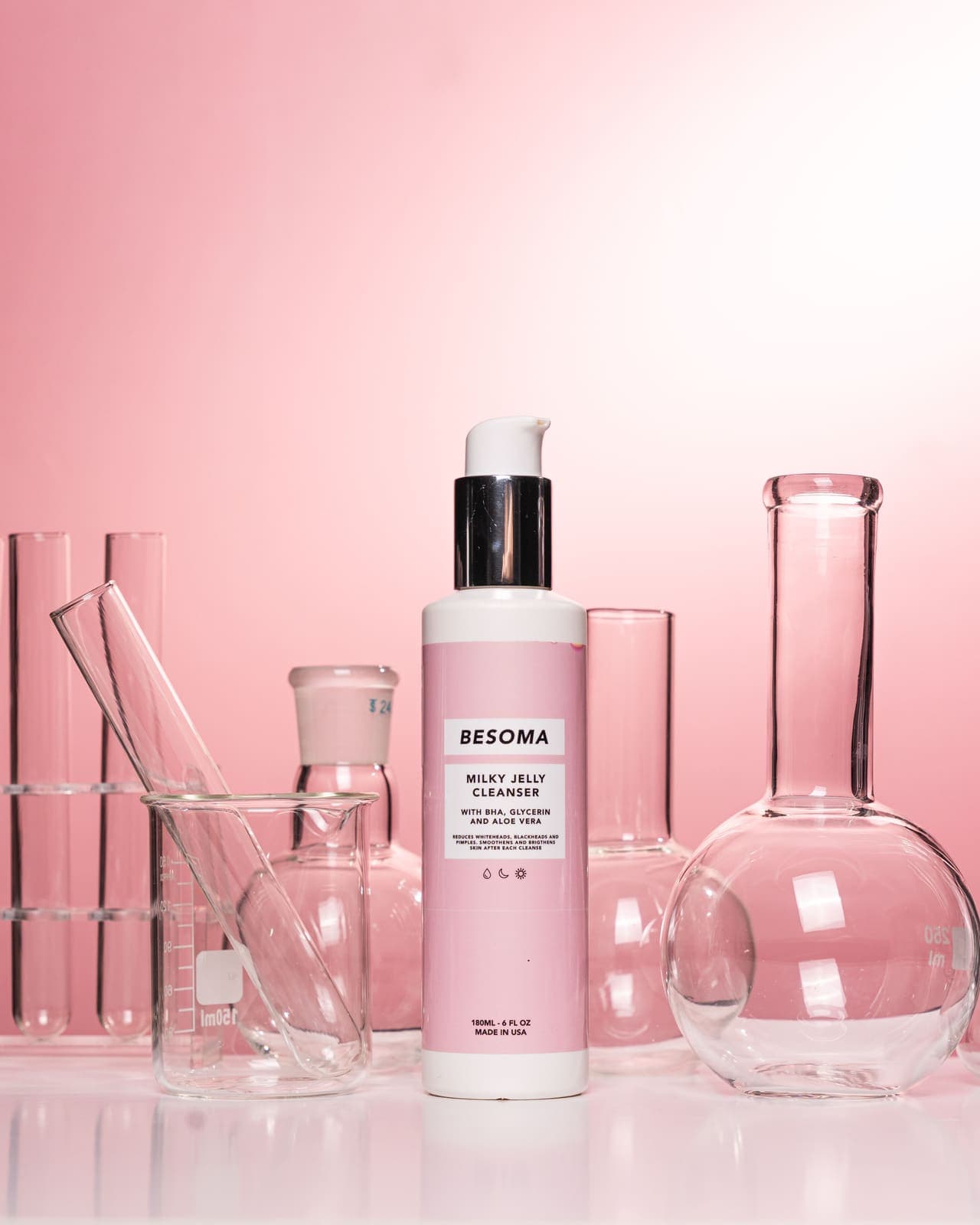 A cleanser bottle styled with laboratory glassware on a pink background.