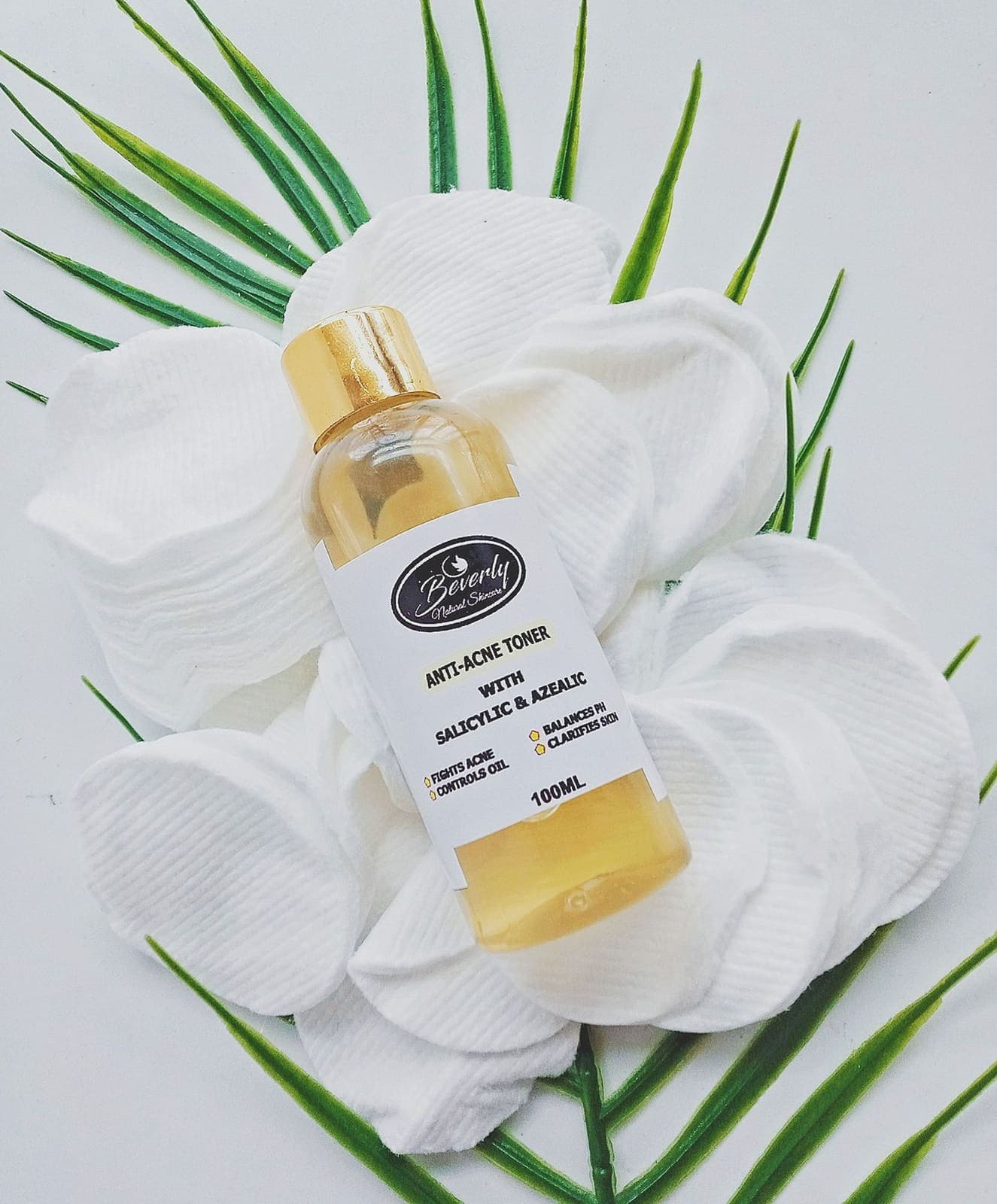 A toner bottle resting on cotton pads with aloe vera leaves.