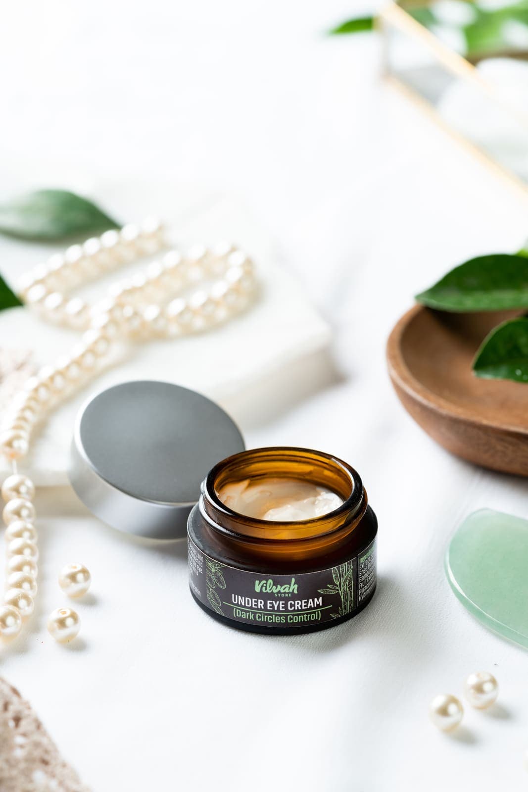 An eye cream jar styled with pearls and leaves.