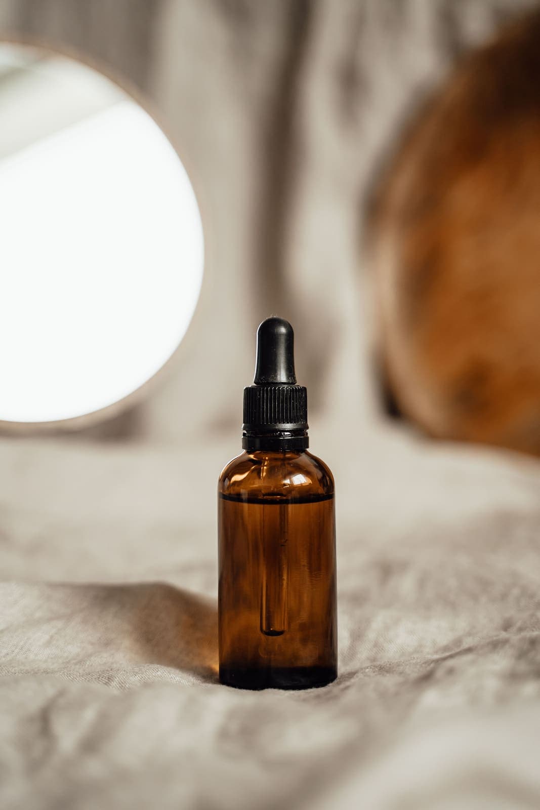 An amber glass dropper bottle of facial oil on soft fabric.