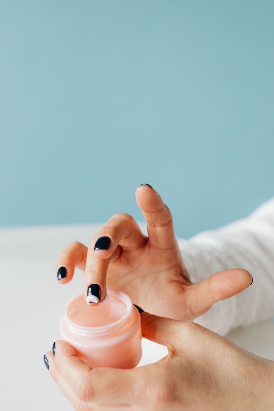 Hands applying moisturizer from a pink jar.