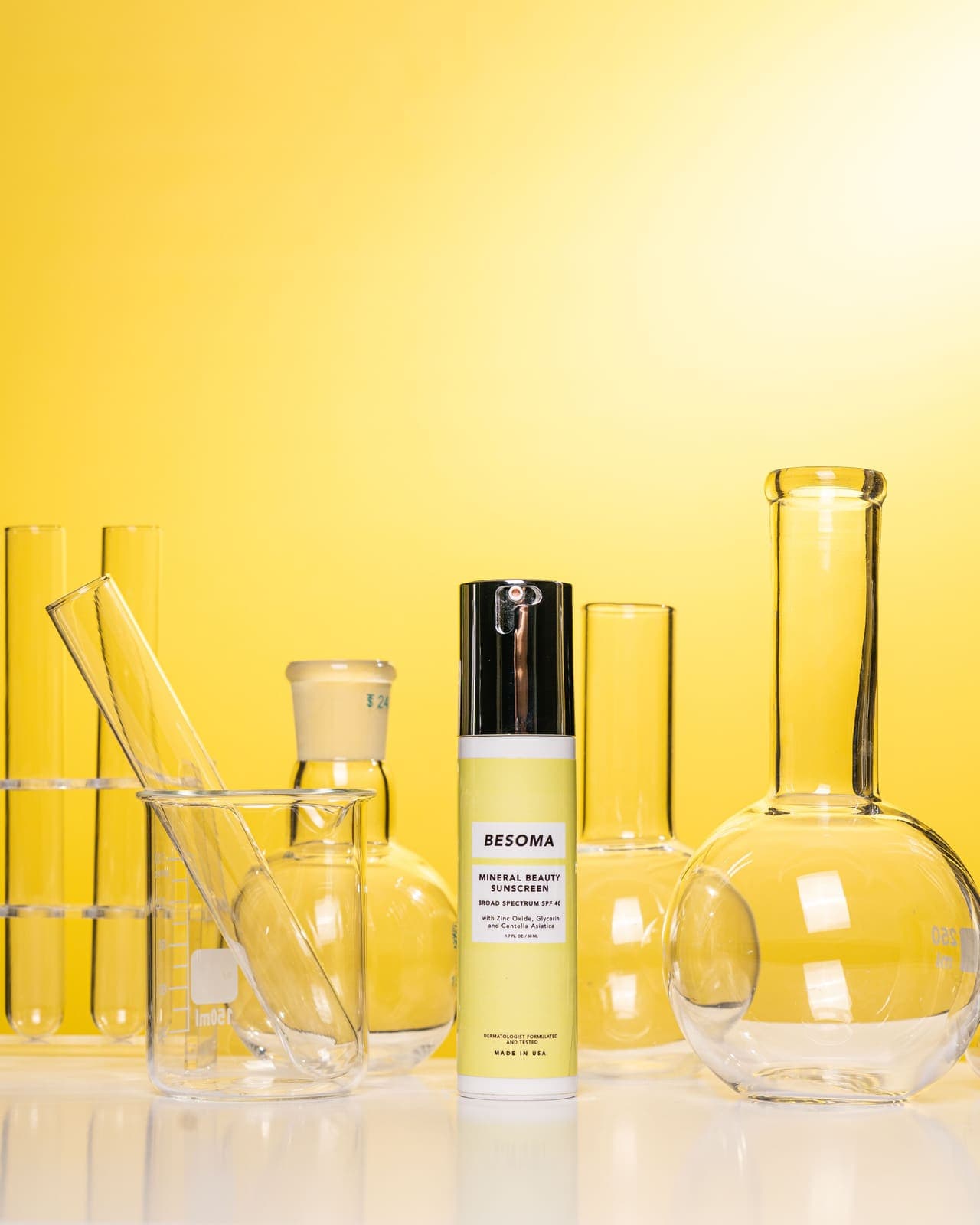 A sunscreen bottle styled with laboratory glassware on a yellow background.