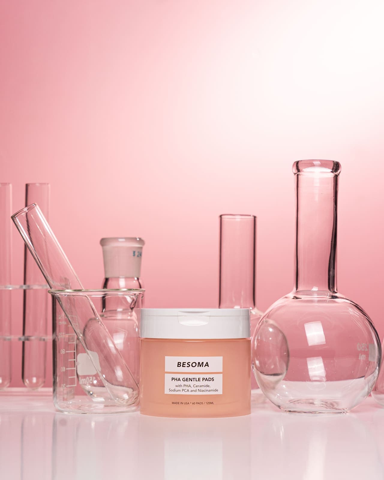 Skincare cream styled with laboratory glassware on a pink background.