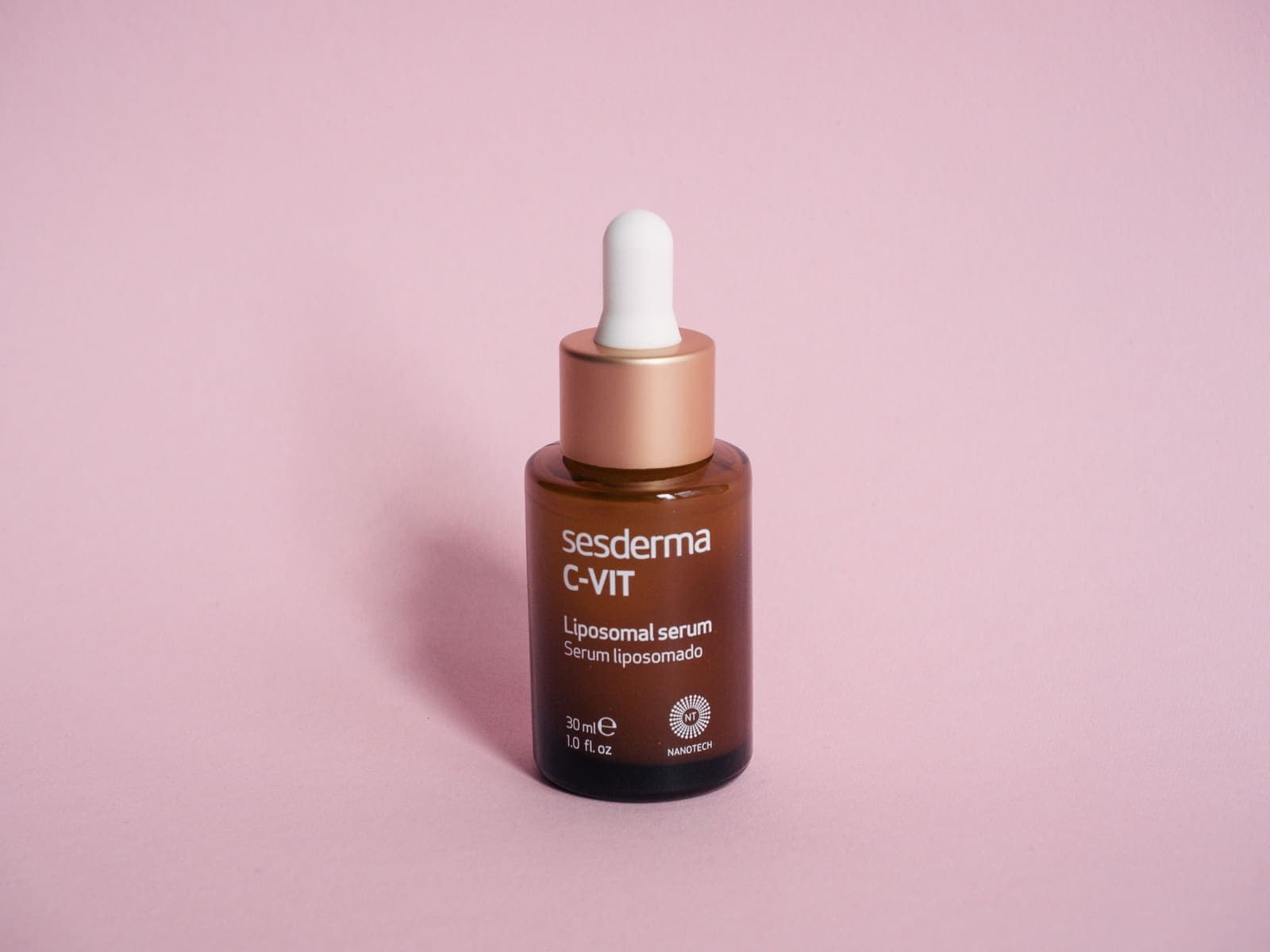 A serum bottle with dropper resting on a pink surface, used to brighten dull skin.